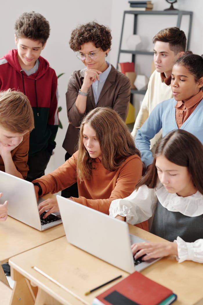 Group of teenagers in a classroom collaboratively working on laptops, fostering team learning.