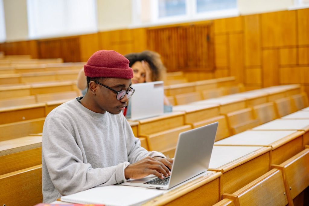 Students focus on laptops in a spacious university lecture hall, learning and working digitally.